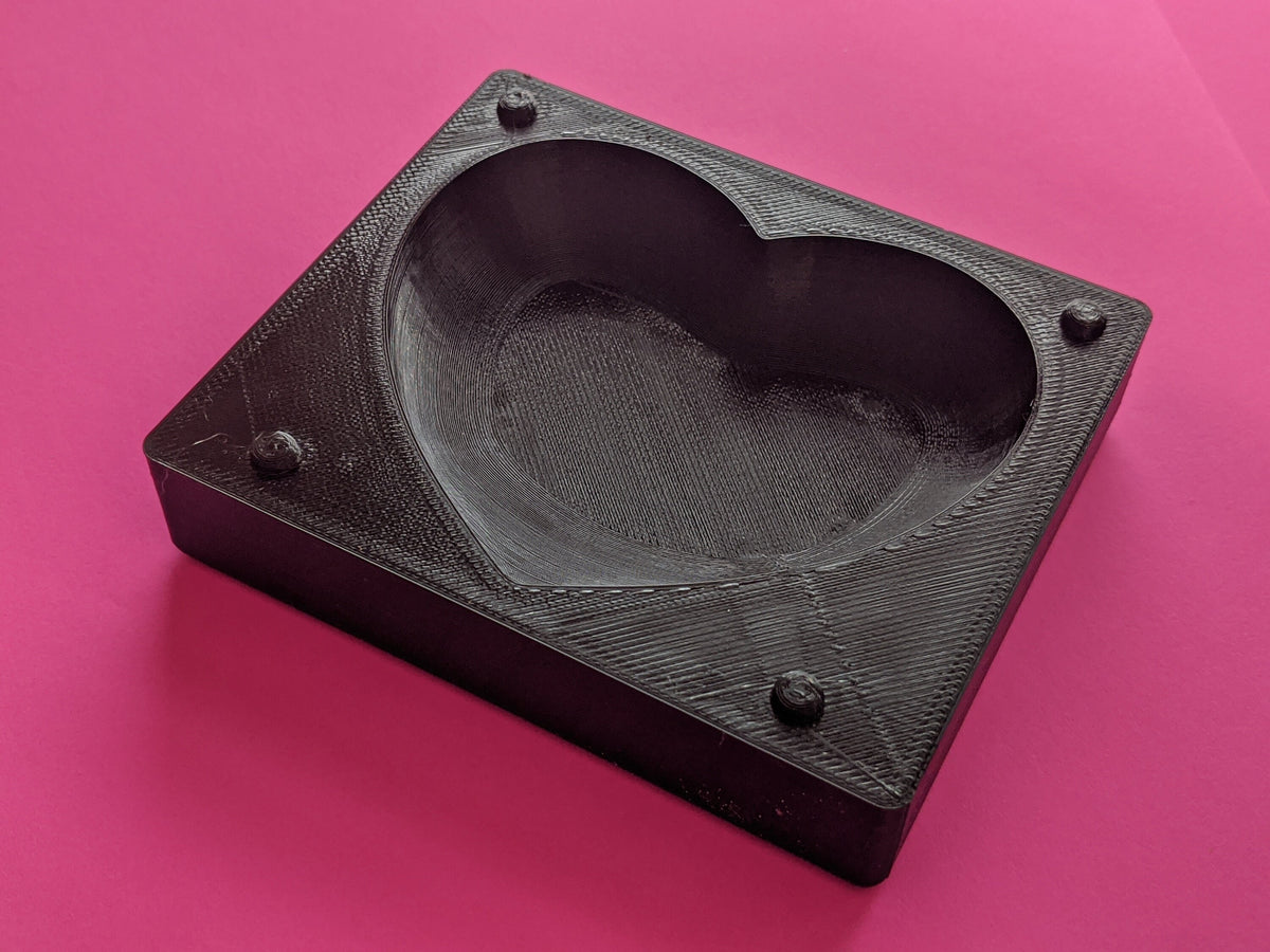 Close view of a dark square heart butter mold half on a pink background, showing the deep cavity and corner alignments.
