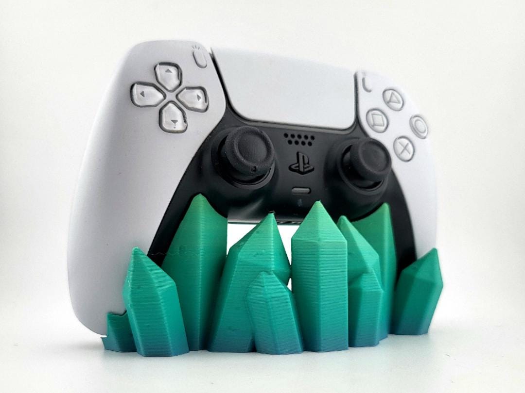 Teal-green crystal-shaped stand holding a PS5 DualSense controller; pictured color example, controller excluded