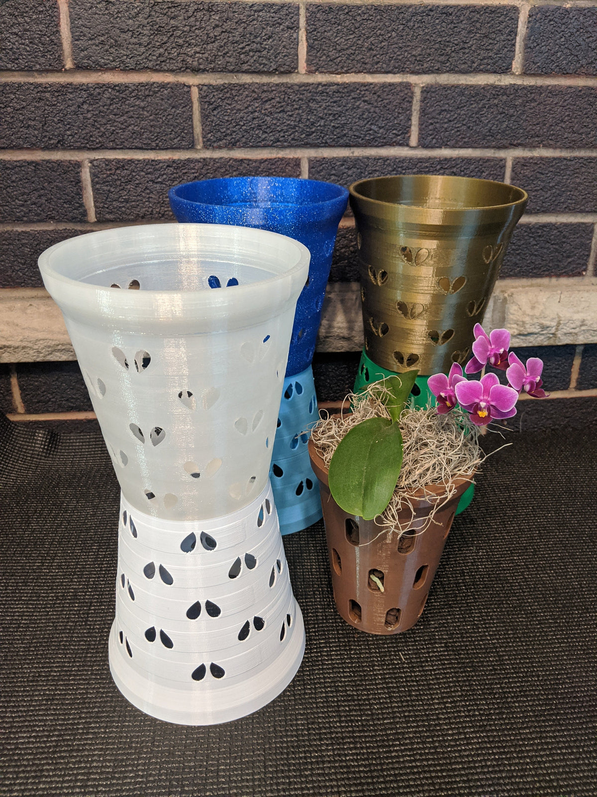 Two clear heart-hole orchid pot liners stacked rim-to-rim with blue, bronze, and brown pots behind them