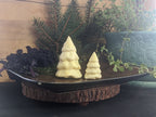 Two Christmas-tree-shaped butter forms on a dark oval tray over a round wood-slice base.