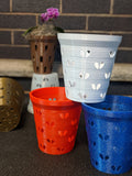 Heart-hole orchid pot liners in white, orange, and blue displayed with additional pots and a small purple orchid