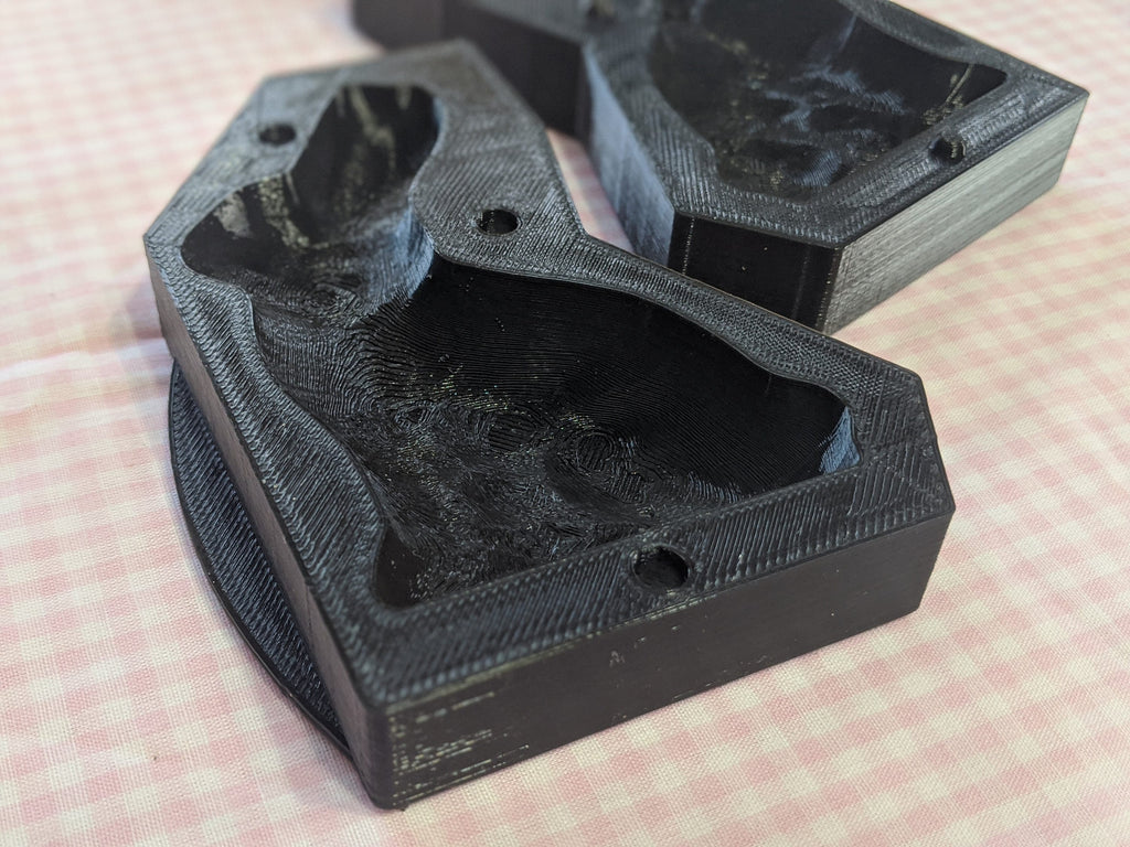 Open black bunny butter mold sections with recessed cavities on pink gingham fabric.