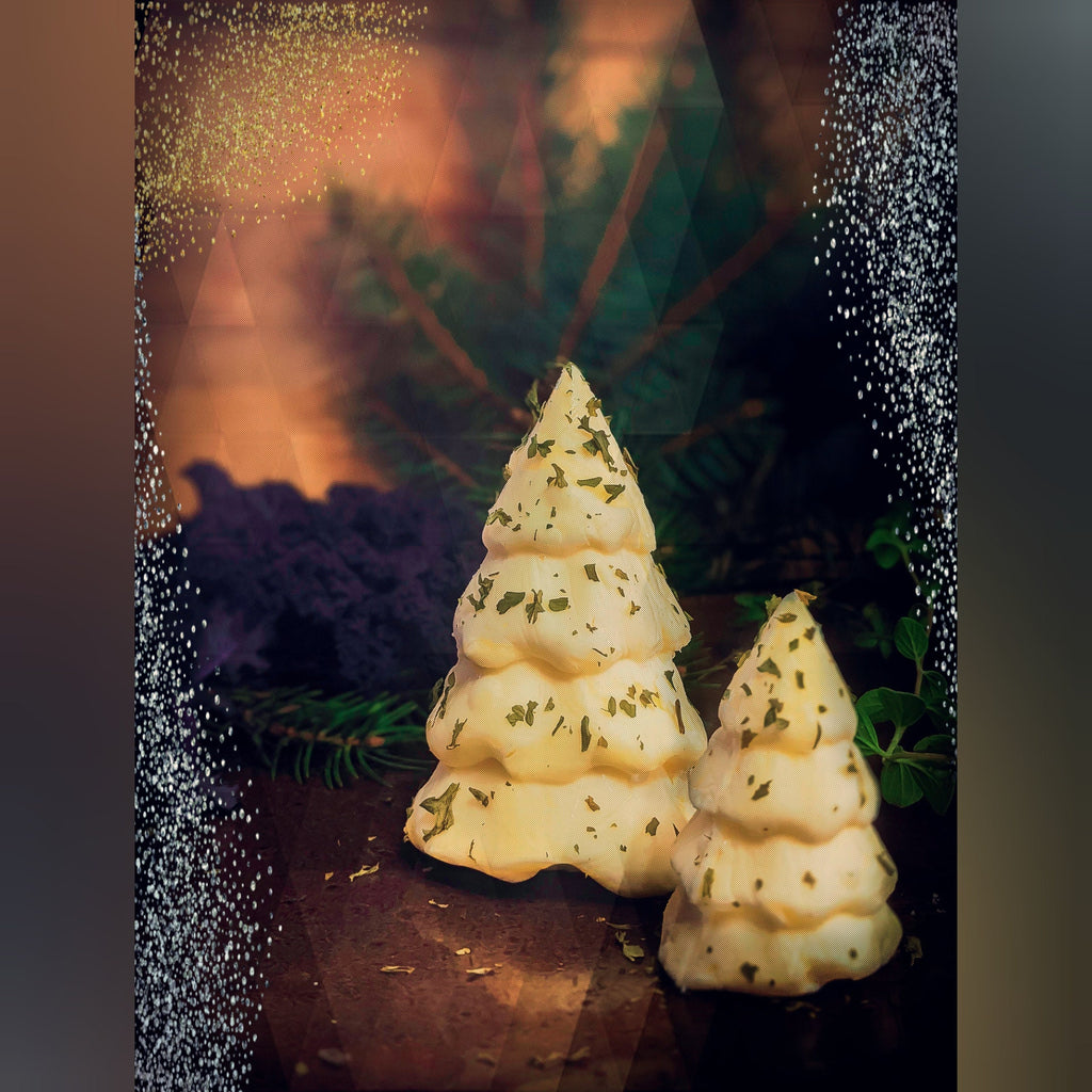 Two Christmas-tree-shaped butter forms with green flecks, staged among evergreen foliage.