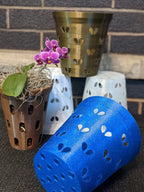 Blue heart-hole orchid pot liner lying beside bronze, white, and brown pots with a small purple orchid