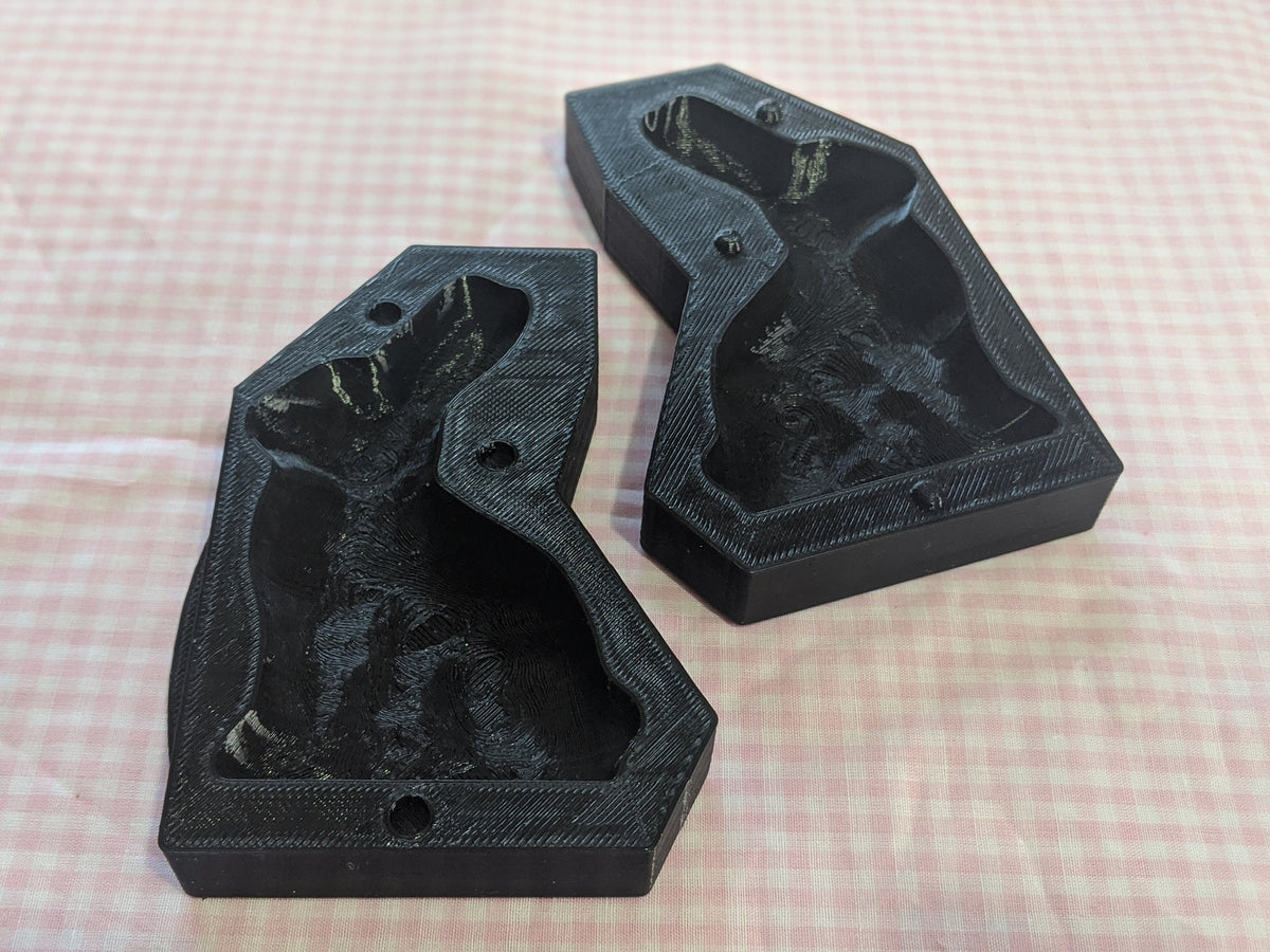 Three black bunny butter mold sections arranged with their cavities facing up on pink gingham.