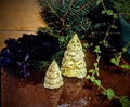 Two Christmas-tree-shaped butter forms with tiered branches and green flecks among holiday greenery.