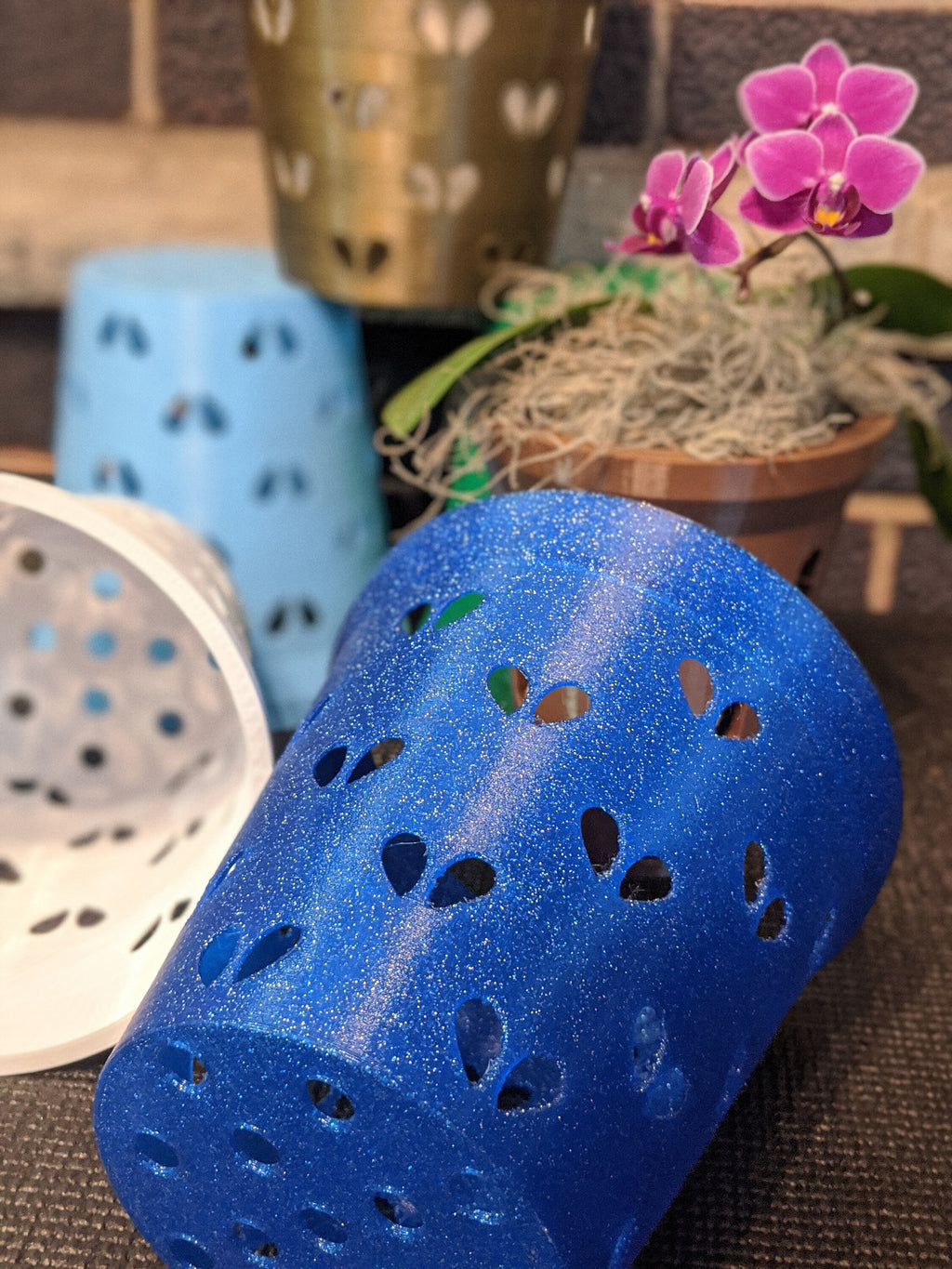 Close-up of a blue glitter heart-hole orchid pot liner lying on its side beside other pots