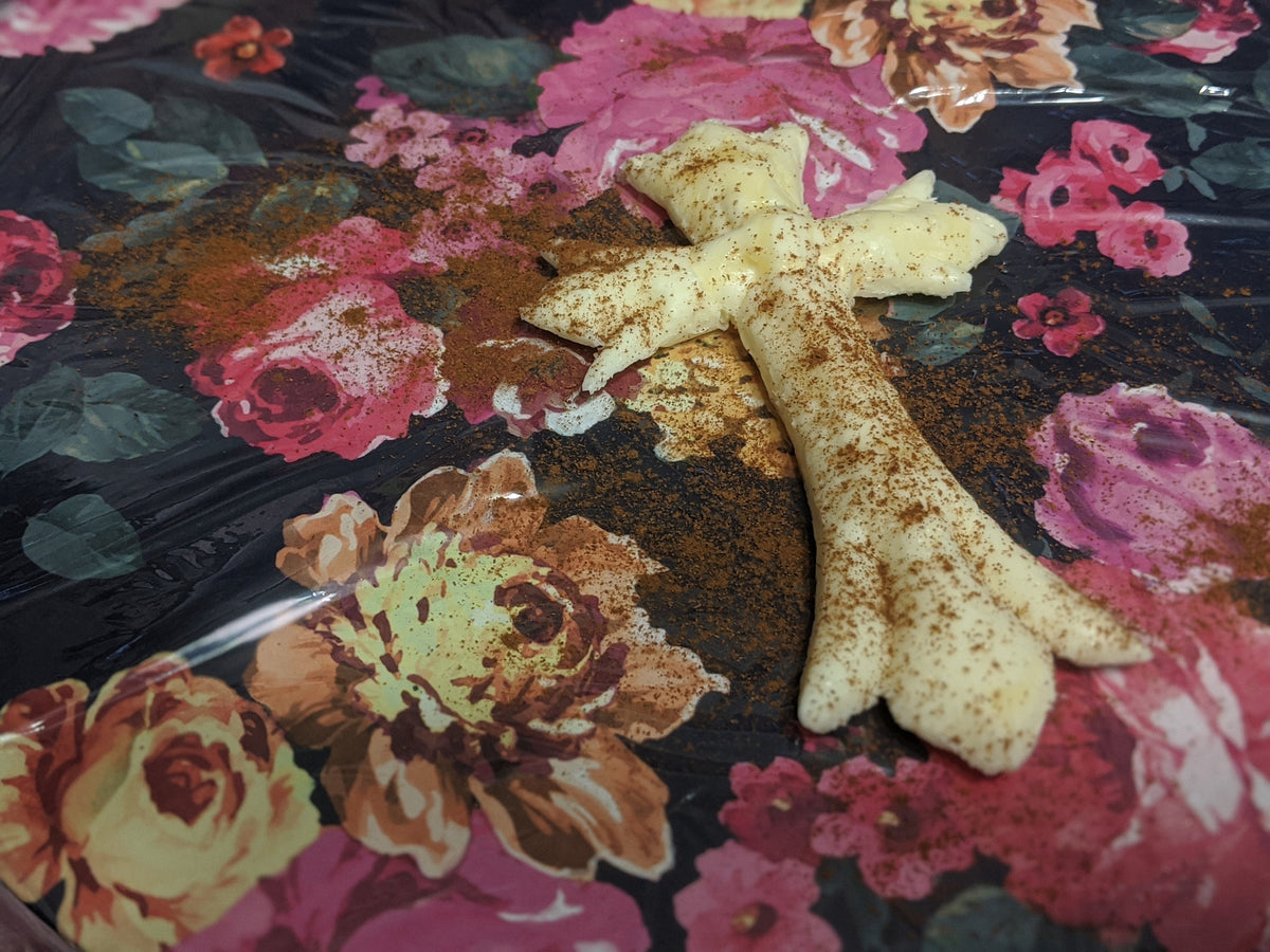 Angled close-up of a pale yellow molded butter cross with decorative contours and scattered brown seasoning on floral print.