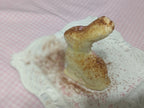 Molded butter figure standing on an ornate white plate dusted with brown powder.