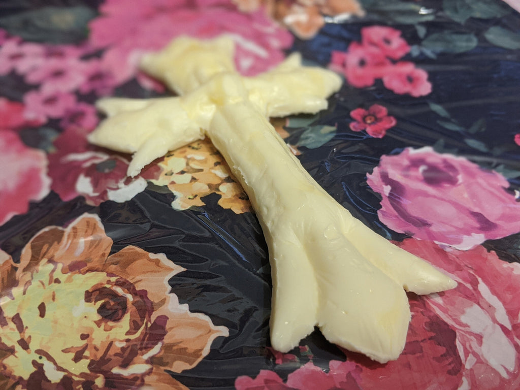 Low close view of a pale yellow molded butter cross on floral print, showing its long curved stem and forked base.