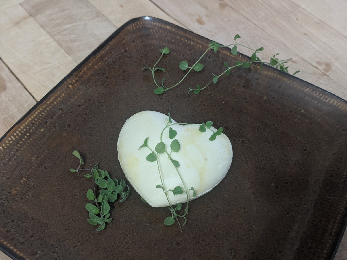 Heart-shaped butter pat with green herb sprigs on a dark brown square plate.