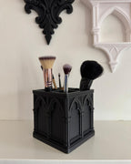 Black Gothic makeup brush organizer with four brushes displayed beneath decorative wall arches