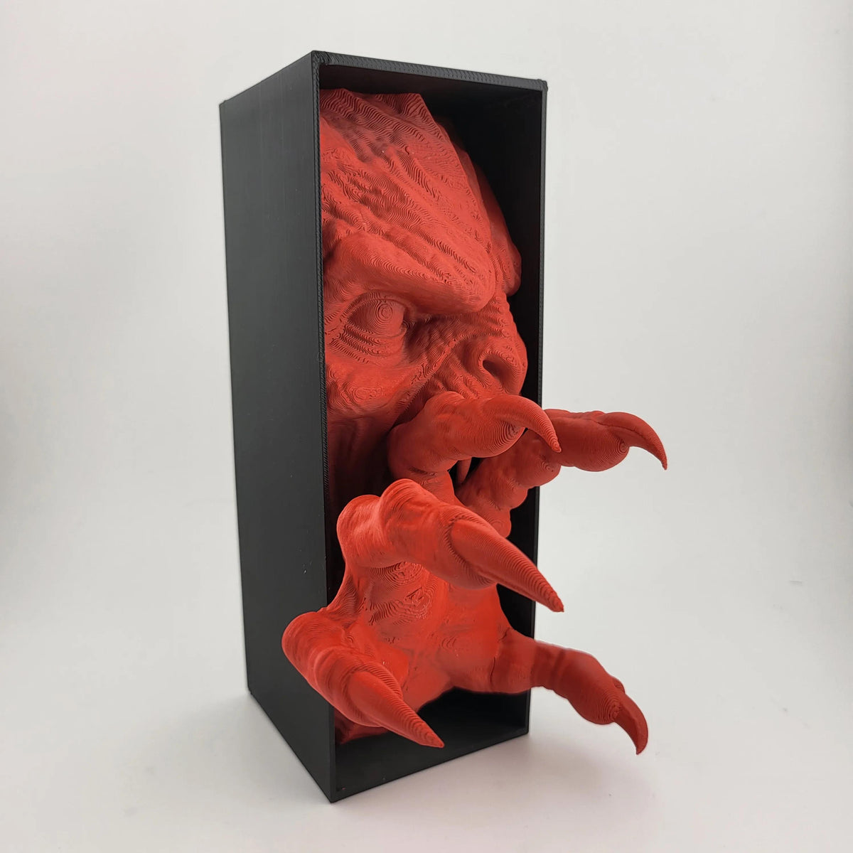 Side view of the red demon face and claw extending from a black box