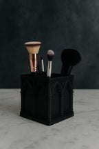 Black cathedral-style brush holder with four brushes on a marble surface against a dark background