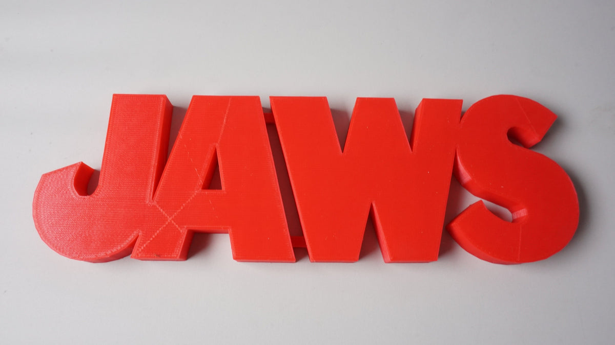 Close elevated front view of the red JAWS shelf sign showing rounded letter edges on a light-gray surface.