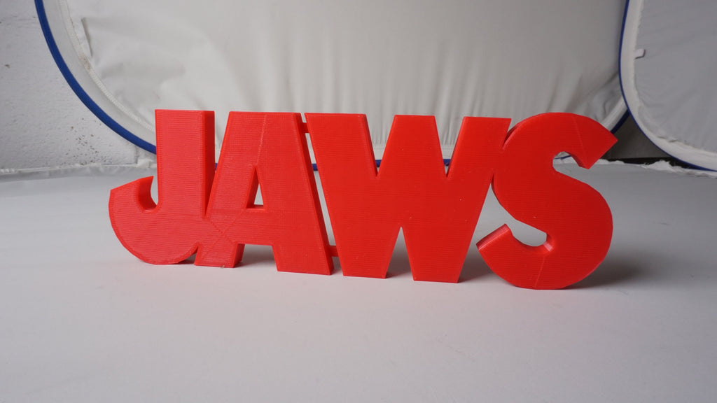 Wide front view of the red JAWS sign against a curved white backdrop with blue trim behind it.