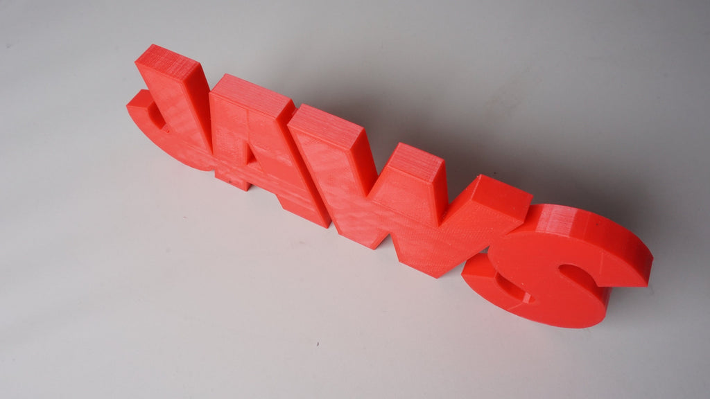 High angled view of the red JAWS sign lying diagonally on a light-gray surface with dark cast shadows.