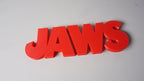 Three-quarter front view of the full red JAWS sign on a pale-gray background.