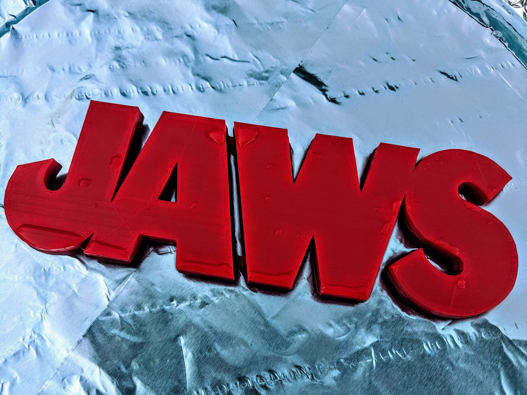 Angled close-up of the red JAWS sign on a wrinkled pale blue-and-white surface.