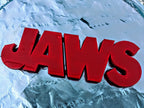 Angled close-up of the red JAWS sign on a wrinkled pale blue-and-white surface.