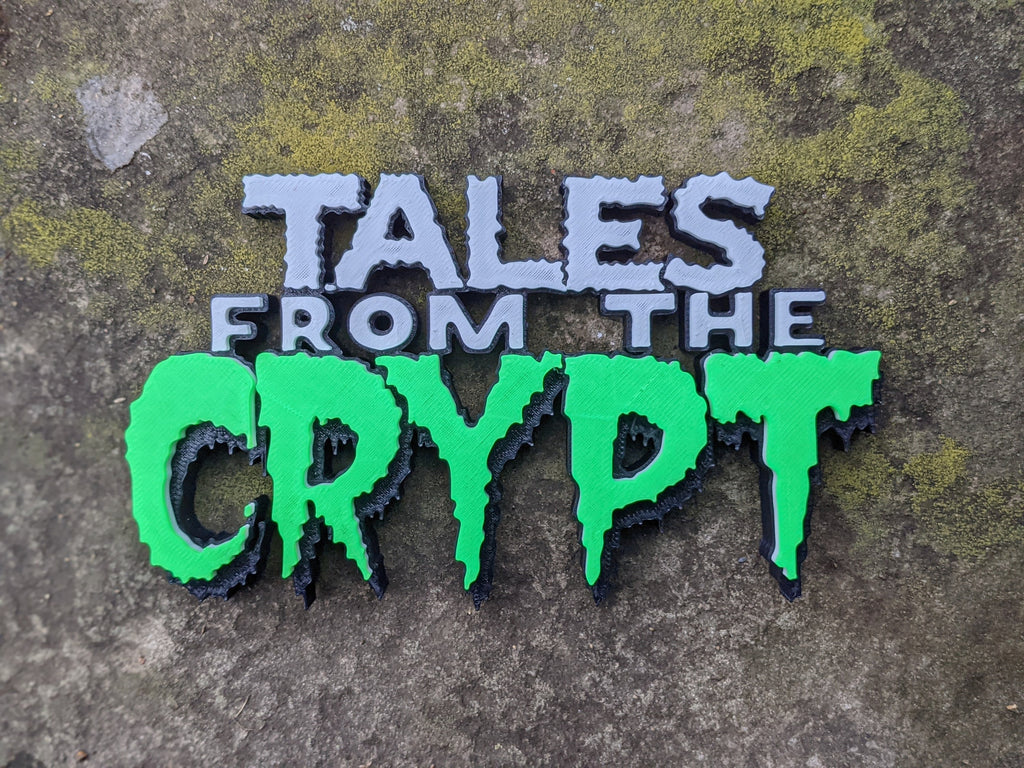 Tales from the Crypt sign with white-gray upper lettering and bright green dripping Crypt letters on mottled stone.