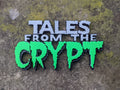 Tales from the Crypt sign with white-gray upper lettering and bright green dripping Crypt letters on mottled stone.