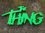 Neon-green The Thing shelf sign with jagged horror lettering, viewed from above on mottled dark stone.