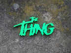 The Thing neon-green logo sign centered in a wider overhead view on weathered gray stone.
