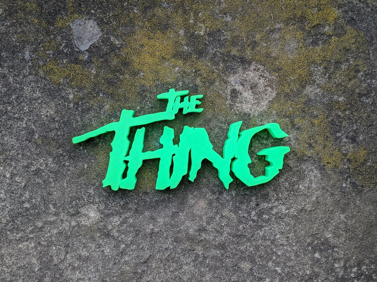 The Thing neon-green logo sign centered in a wider overhead view on weathered gray stone.