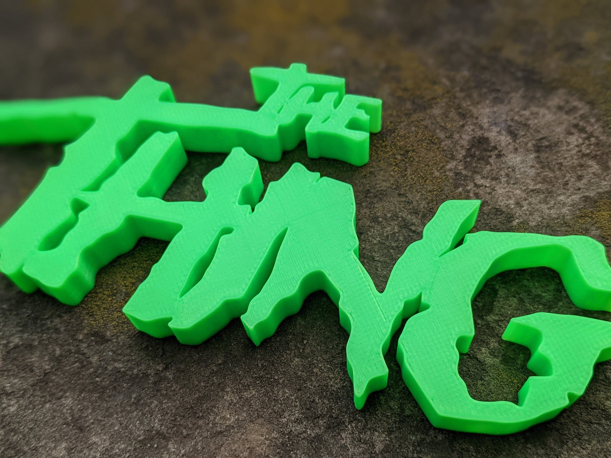 Low close-up of The Thing sign showing thick green letters, pointed edges and shadows on a dark surface.
