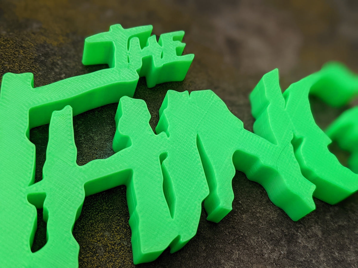 Extreme angled close-up of The Thing sign’s green lettering, showing jagged forms and fine surface layers.